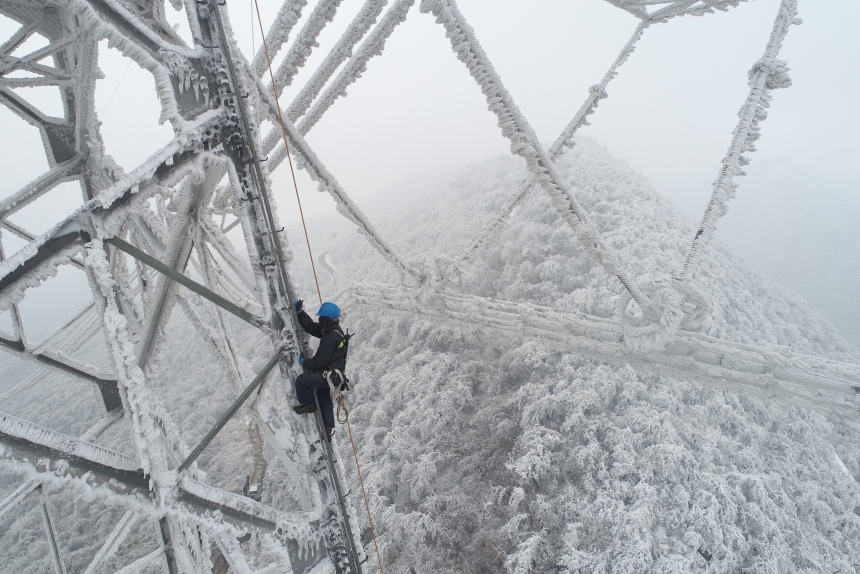 電力應(yīng)急處置人員爬上70米高的±800千伏陜武輸電線路1898號(hào)塔，通過(guò)機(jī)械震動(dòng)方式清除地線和光纜上的積雪。鄒小民攝 